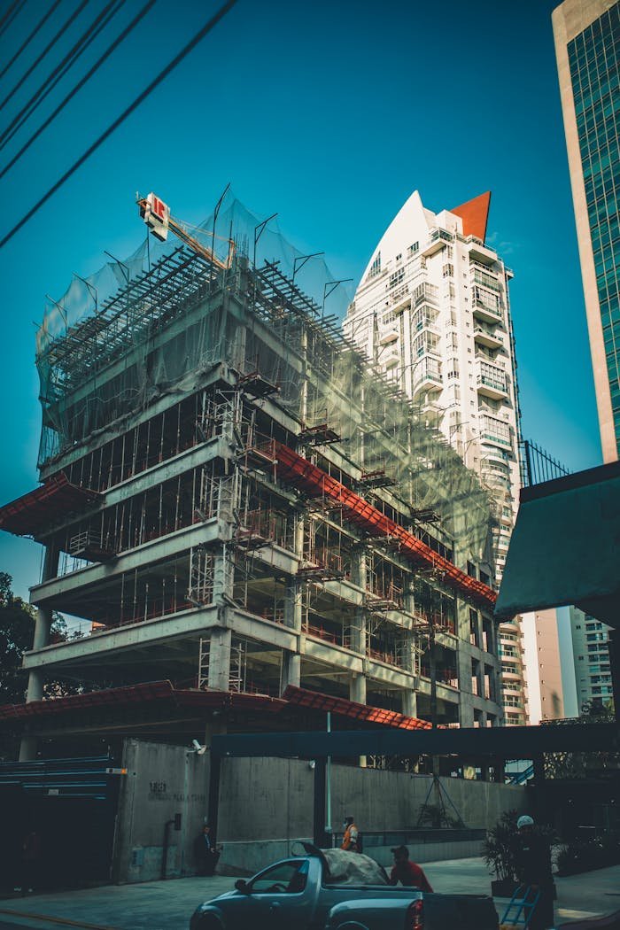 Servicios de construcción en Mallorca. High-rise building under construction with scaffolding and crane in urban cityscape.