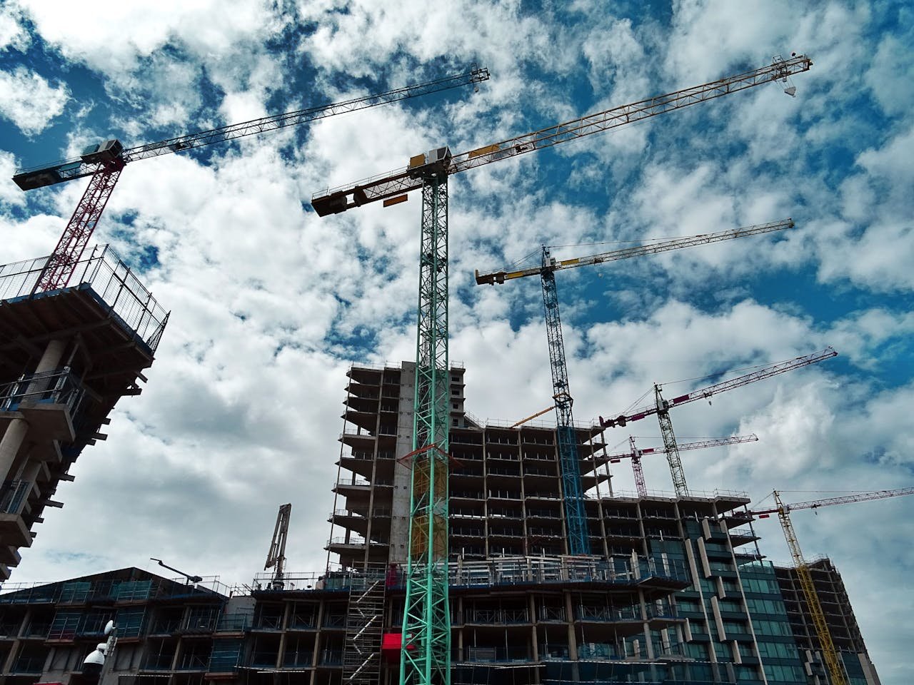 Servicios de construcción en Mallorca. Urban construction site with numerous cranes framing rising skyscrapers against a blue sky.